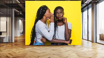 Portrait of two happy young african women sharing secrets isolated over yellow background Wall mural